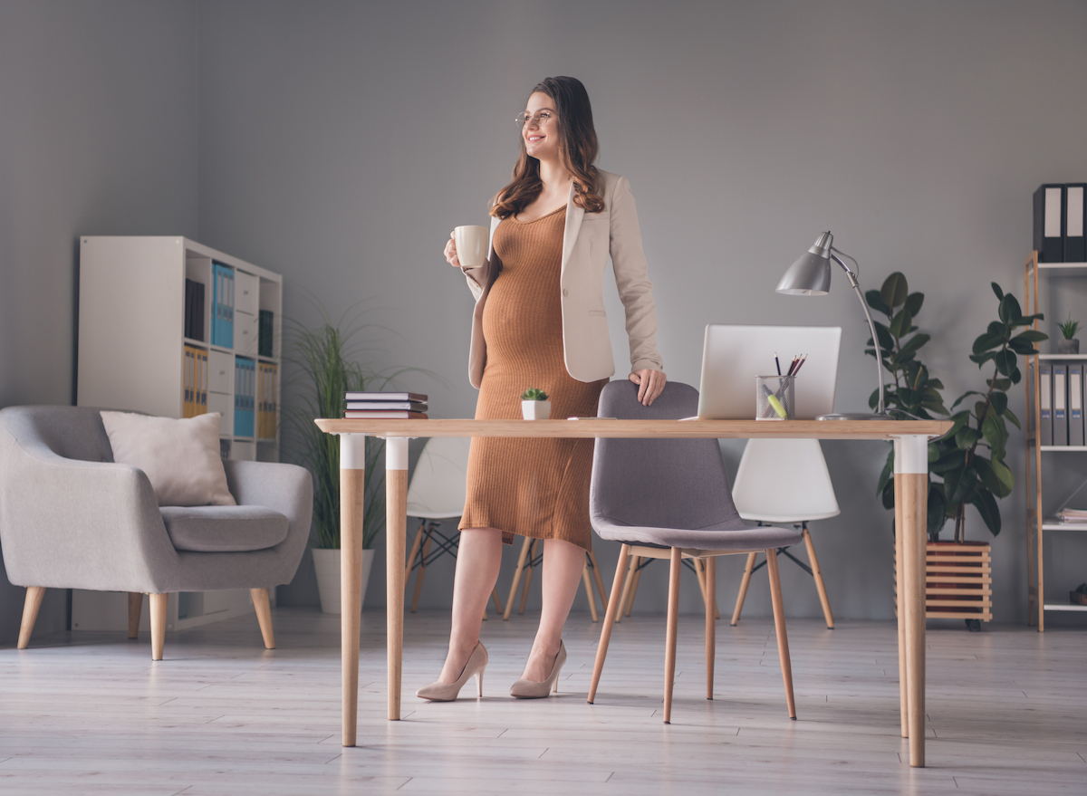 pregnant woman standing at desk with cup of coffee