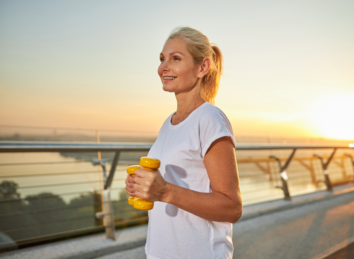 happy woman exercises walking at sunset with dumbbells