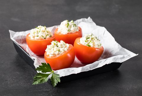 tomatoes stuffed with cottage cheese with parsley in a serving plate on a dark gray background