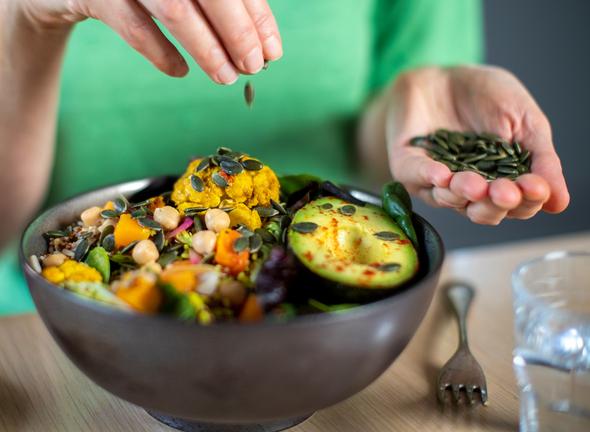 woman adding pumpkin seeds to a salad bowl vegetables avocado plant based food