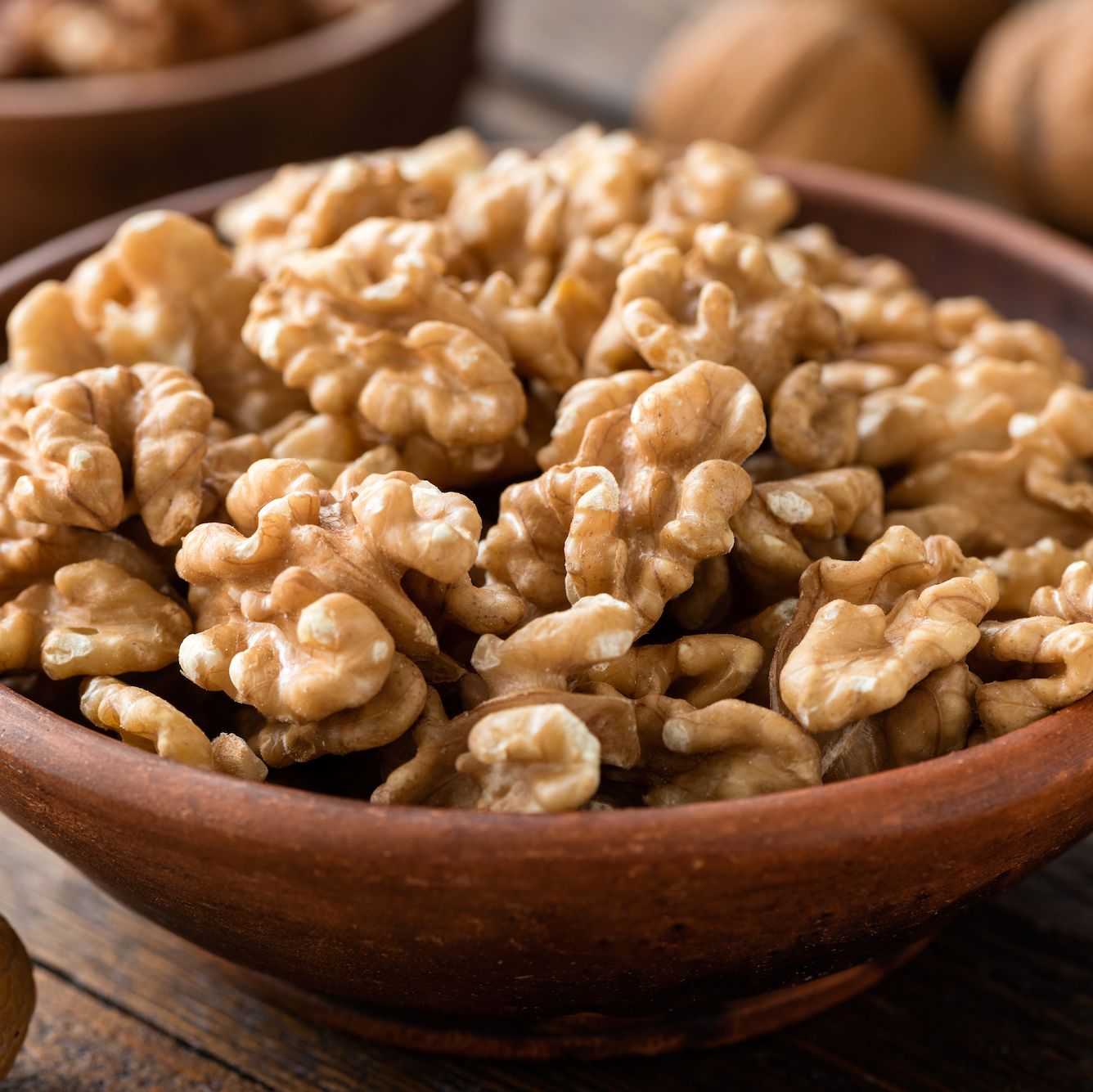 walnuts in brown bowl on wooden table, closeup view healthy food