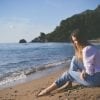 This shows a sad woman sitting on a beach.