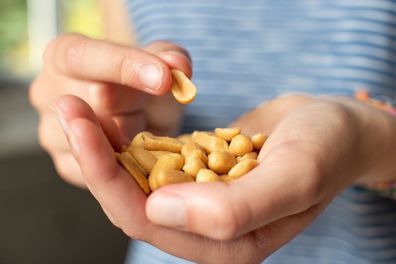 Close up of a teenage girl eating a handful of salted peanuts