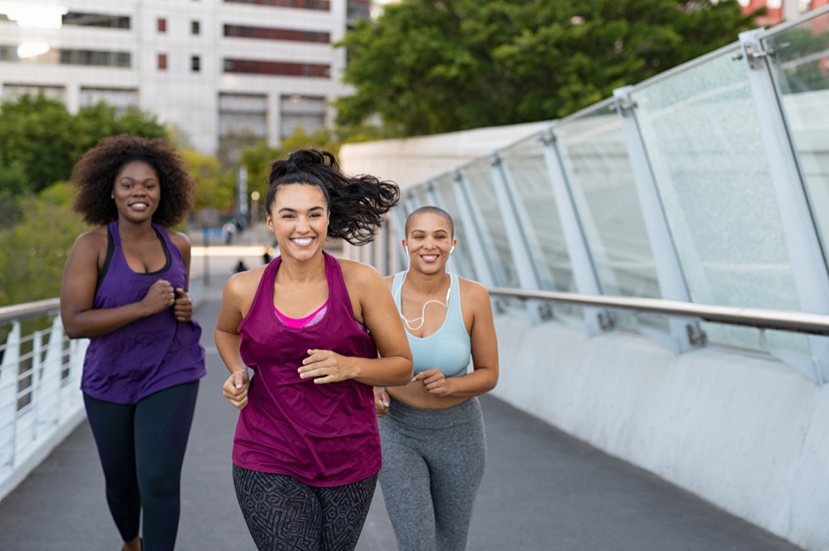 Curvy multiethnic young women jogging together on city bridge