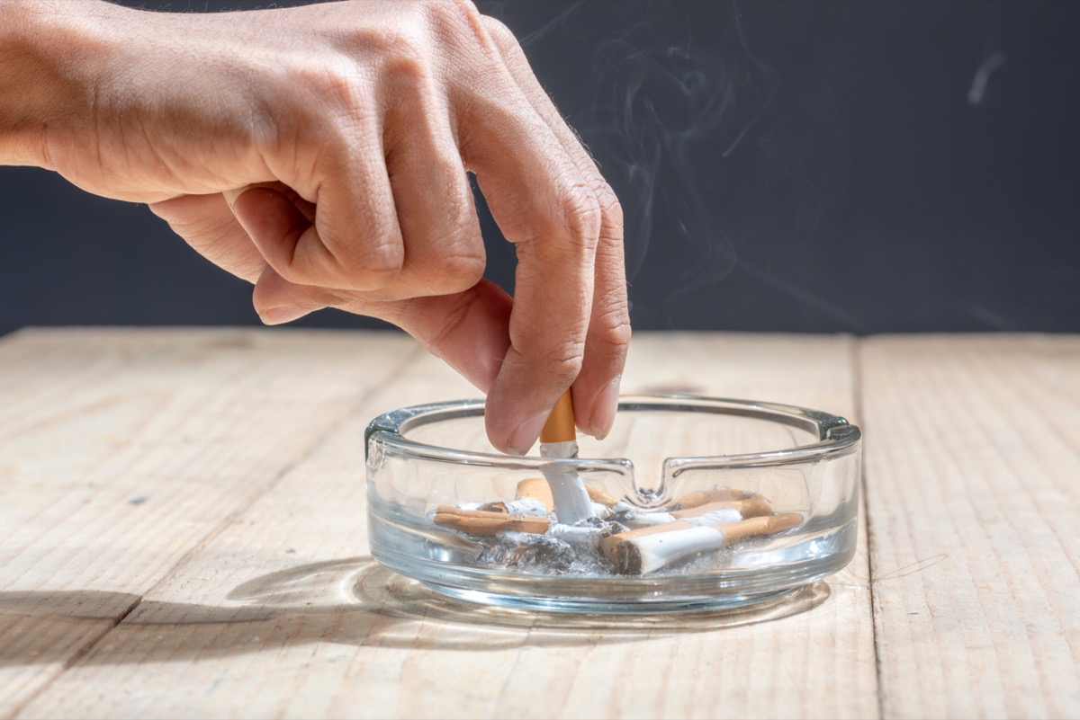 Hand put out cigarette in transparent ashtray on wooden table