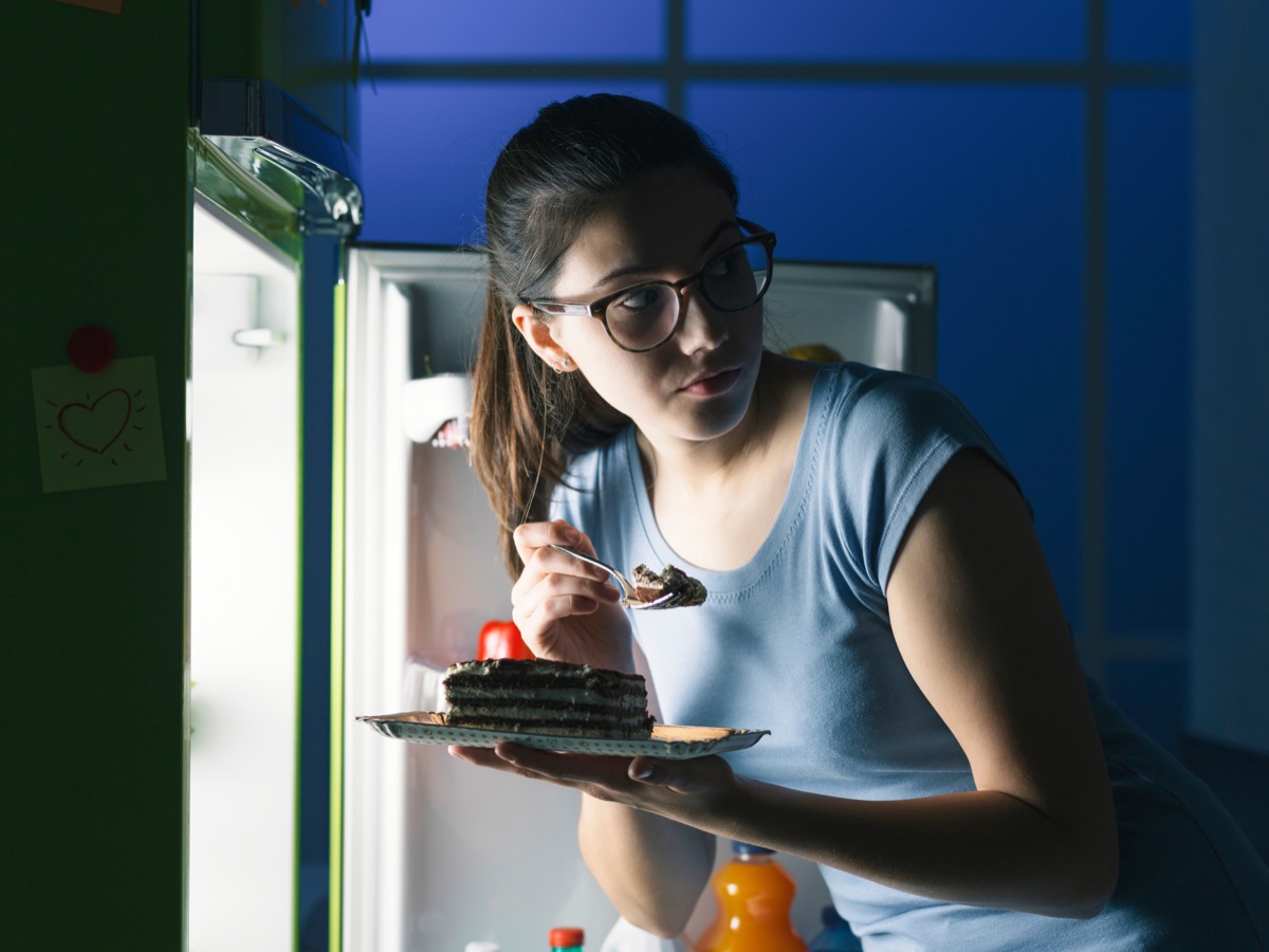 Woman sneaking into the fridge to eat a cake late at night hoping not to get caught