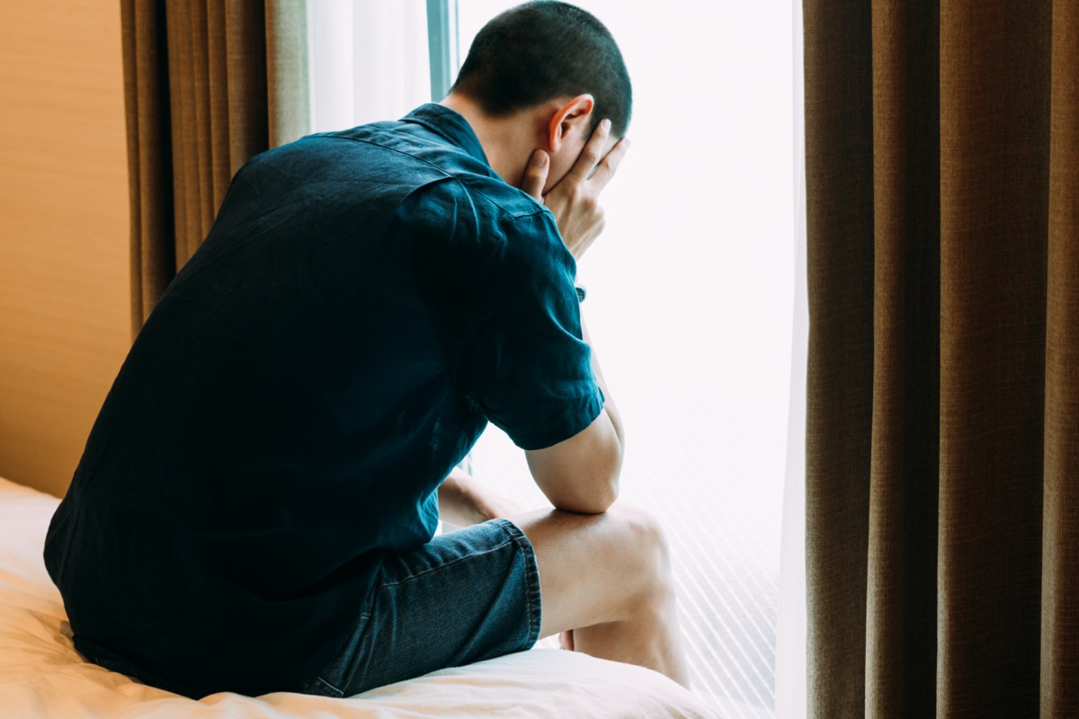 Troubled depressed man sitting alone with head in hands in bed and crying