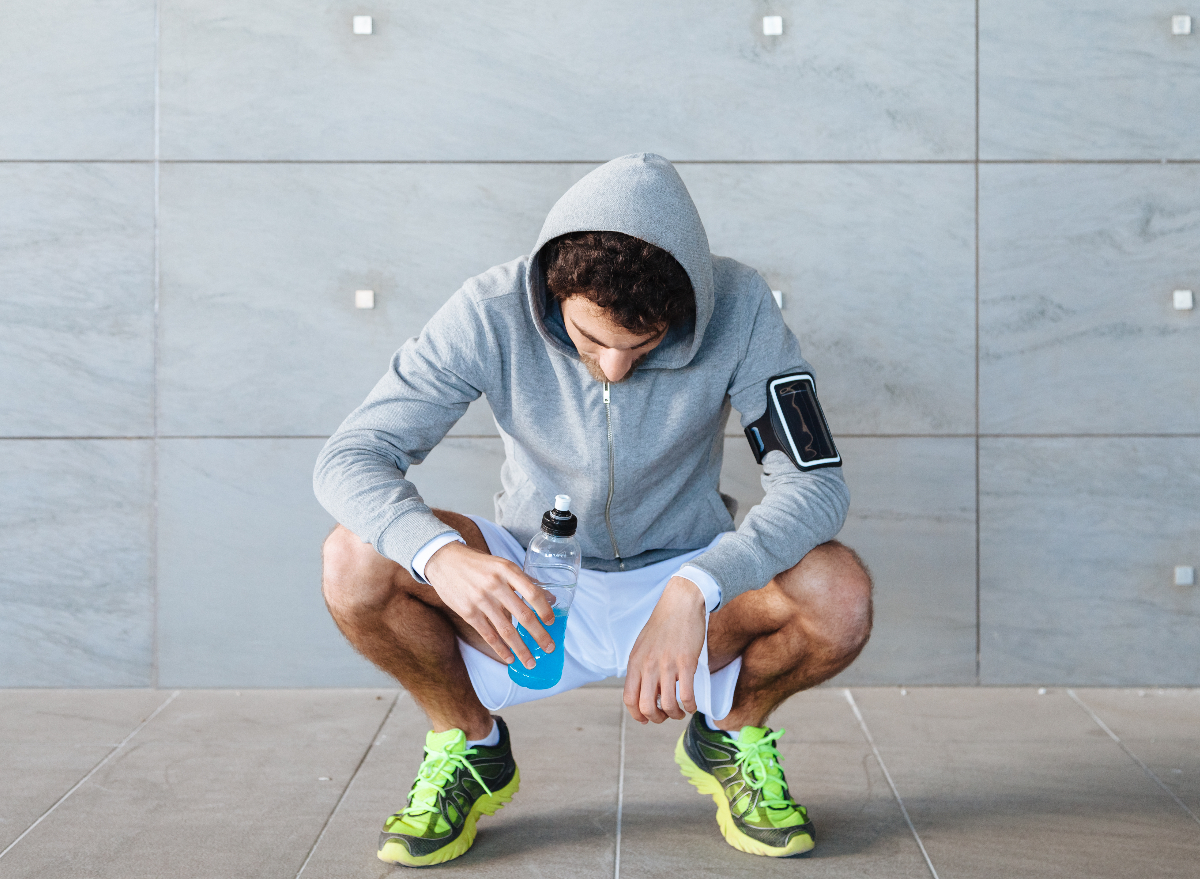 kneeling man holding energy drink after workout