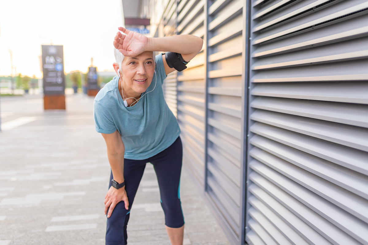 Tired senior woman after jogging.  Tired senior woman resting after jogging outdoors.  African female runner standing with hands on knees.  Fitness sport woman resting after an intense night run