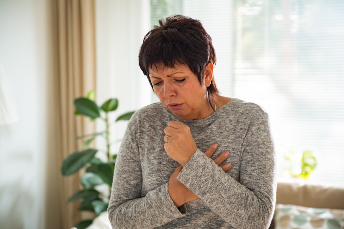 Mature woman with a sore throat, standing in the living room at home.