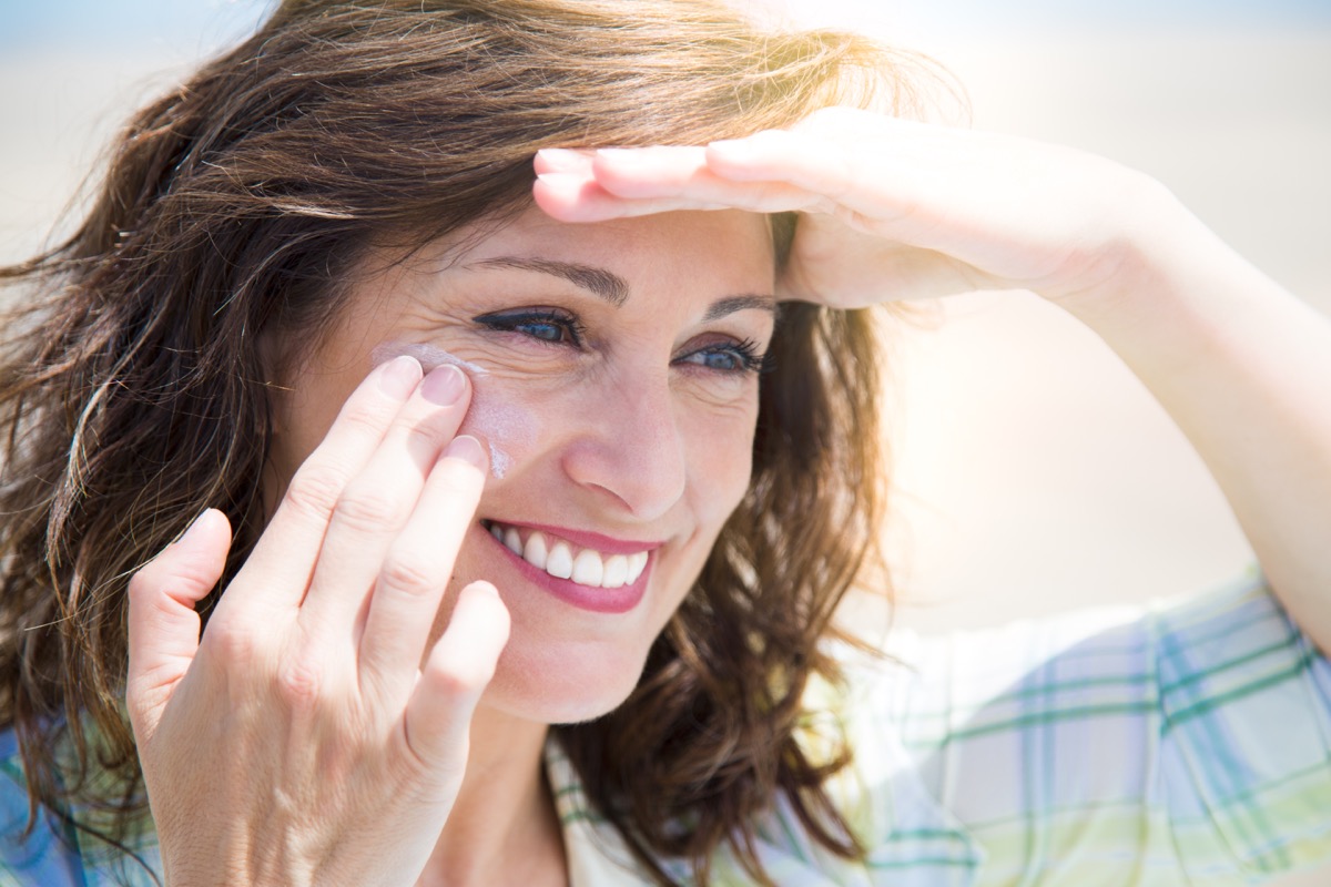 middle aged woman applying sunscreen lotion on her face at the beach