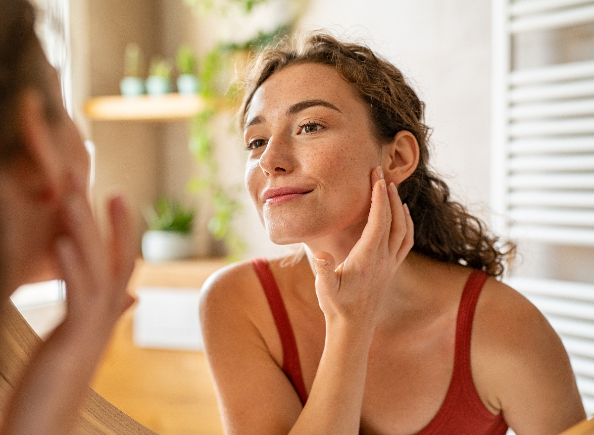 happy woman looks at clear complexion in the mirror