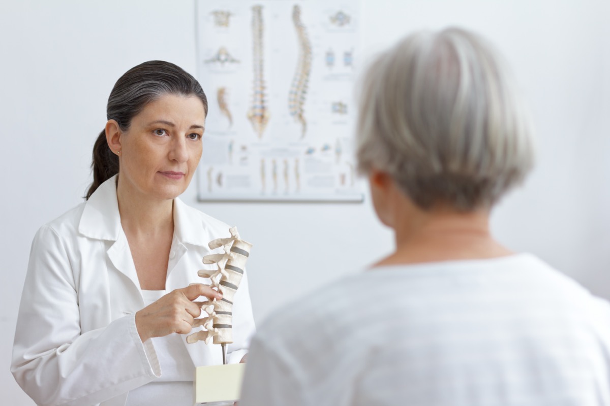 Orthopedic doctor showing an older patient a herniated disc on a spinal column model.