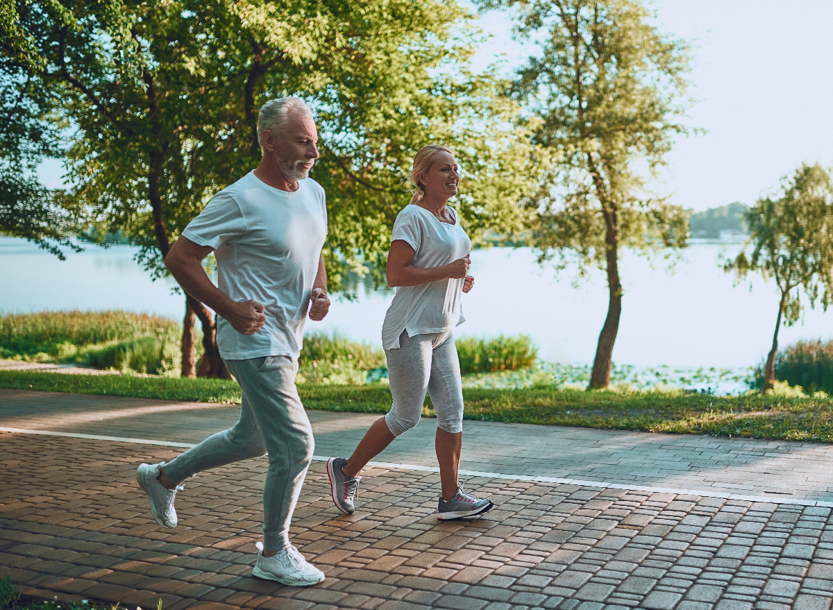 mature couple running outdoors by the lake, demonstrating cardio habits that age you faster