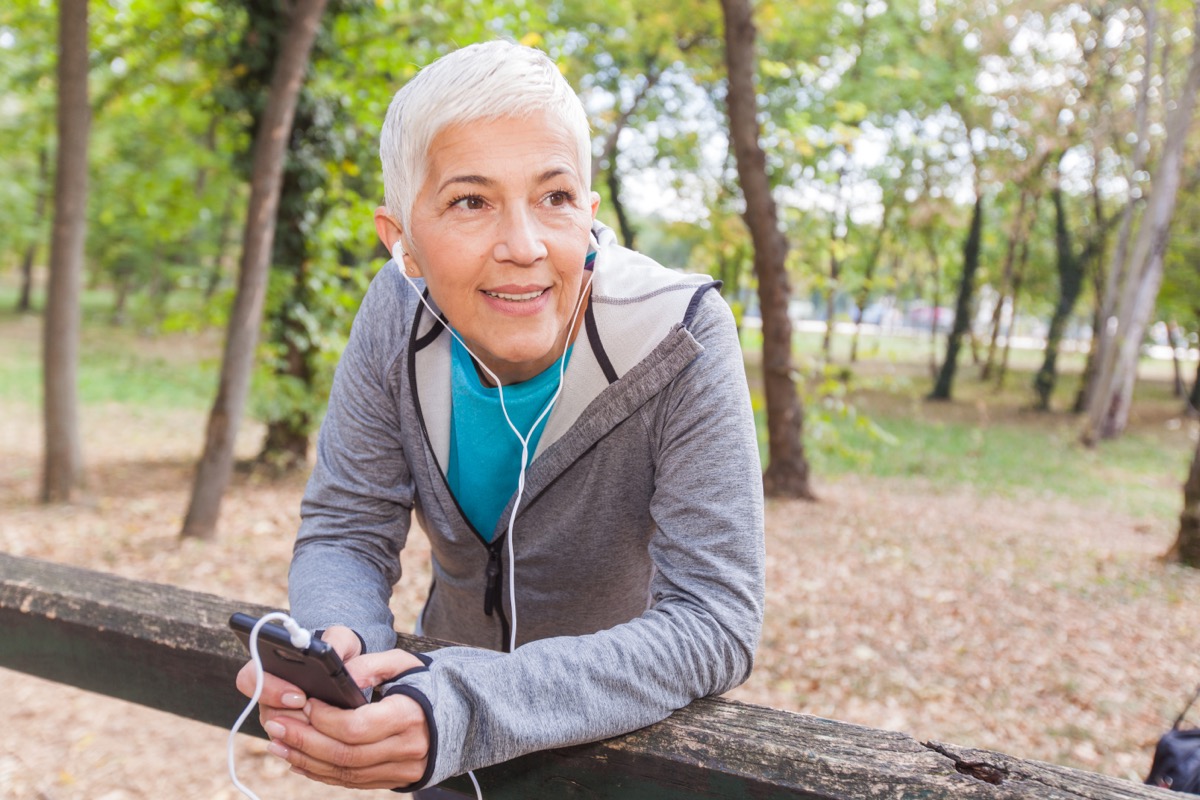 Senior woman relax listening to music with phone after jogging in forest.  Fit Lifestyle Mature People Training Outdoors.