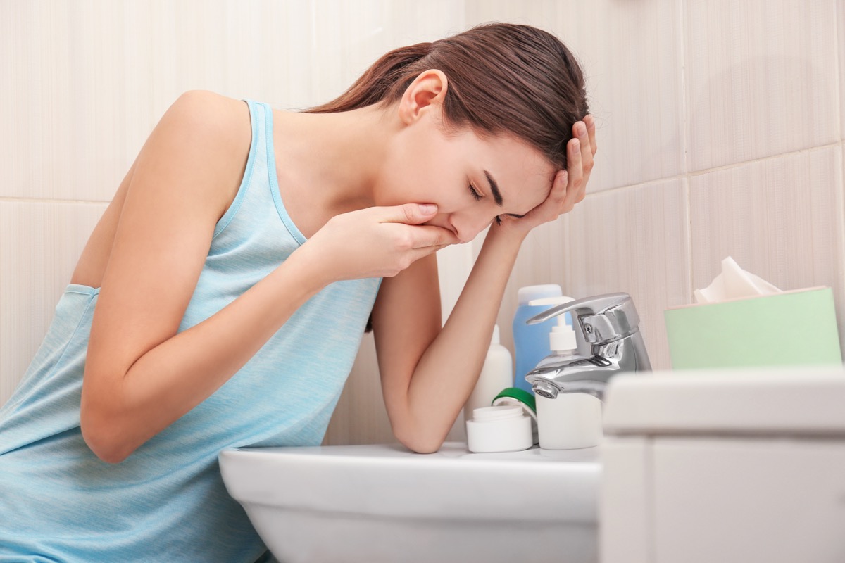 Young woman vomiting near sink in bathroom.