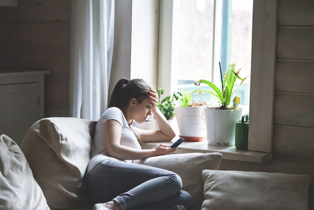 Woman sitting on the bed looking at the phone bored and in a bad mood