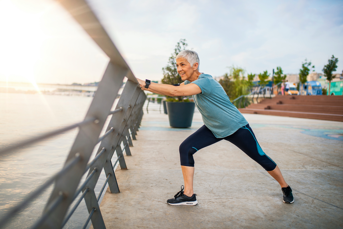 An elderly woman stretches during her workout.  Mature woman exercising.  Portrait of a fit senior woman doing stretching exercise in the park.  Senior sportsman doing stretching exercises