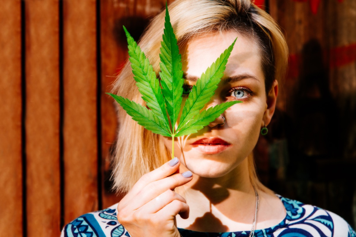 Woman with a cannabis leaf in front of her face.