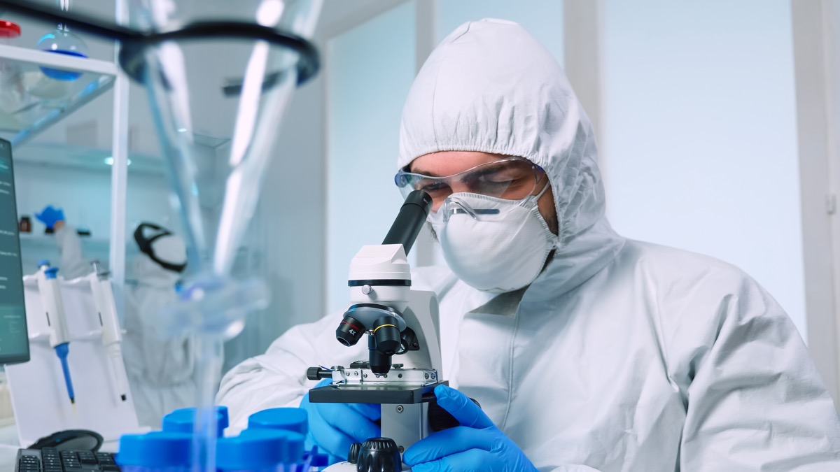 Biotech scientist in ppe suit researching DNA in laboratory using microscope.  equipment examining the evolution of the virus using high technology for the scientific research of the development of vaccines against covid19