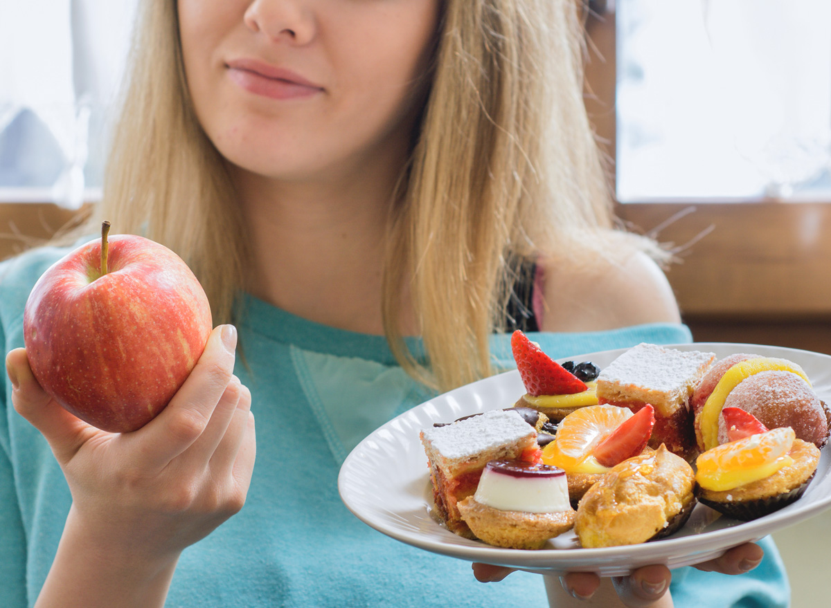 woman choosing healthy apple instead of junk dessert as food swap to reduce calories