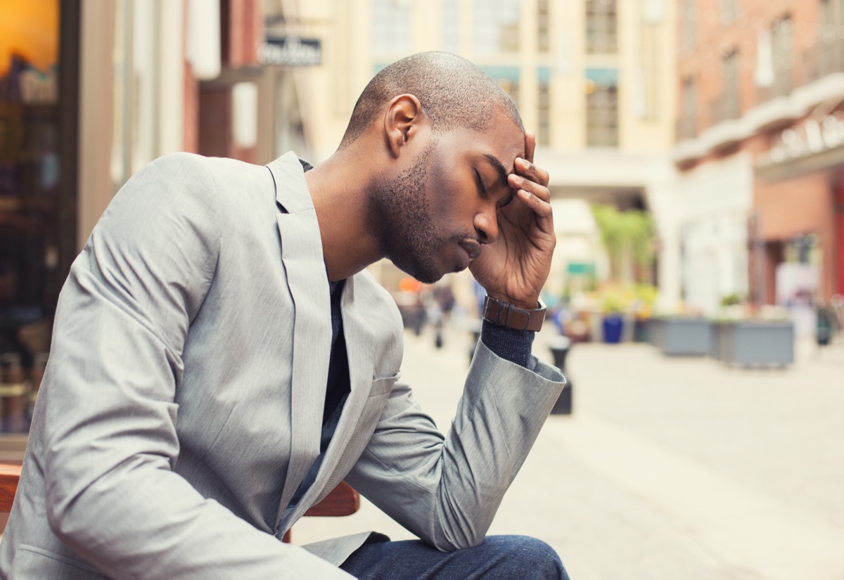 Man in his 20s or 30s in gray jacket and jeans looking depressed outdoors