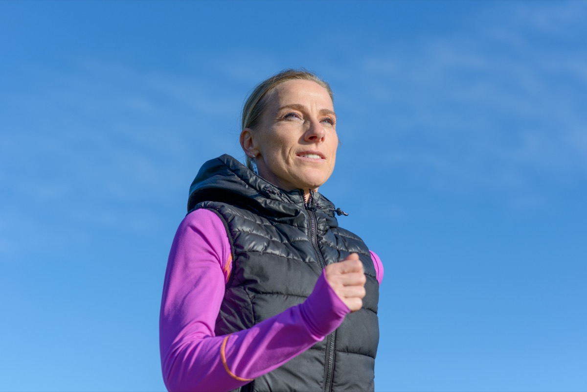 middle aged woman jogging in winter in a low angle view against a sunny blue sky in a healthy active lifestyle