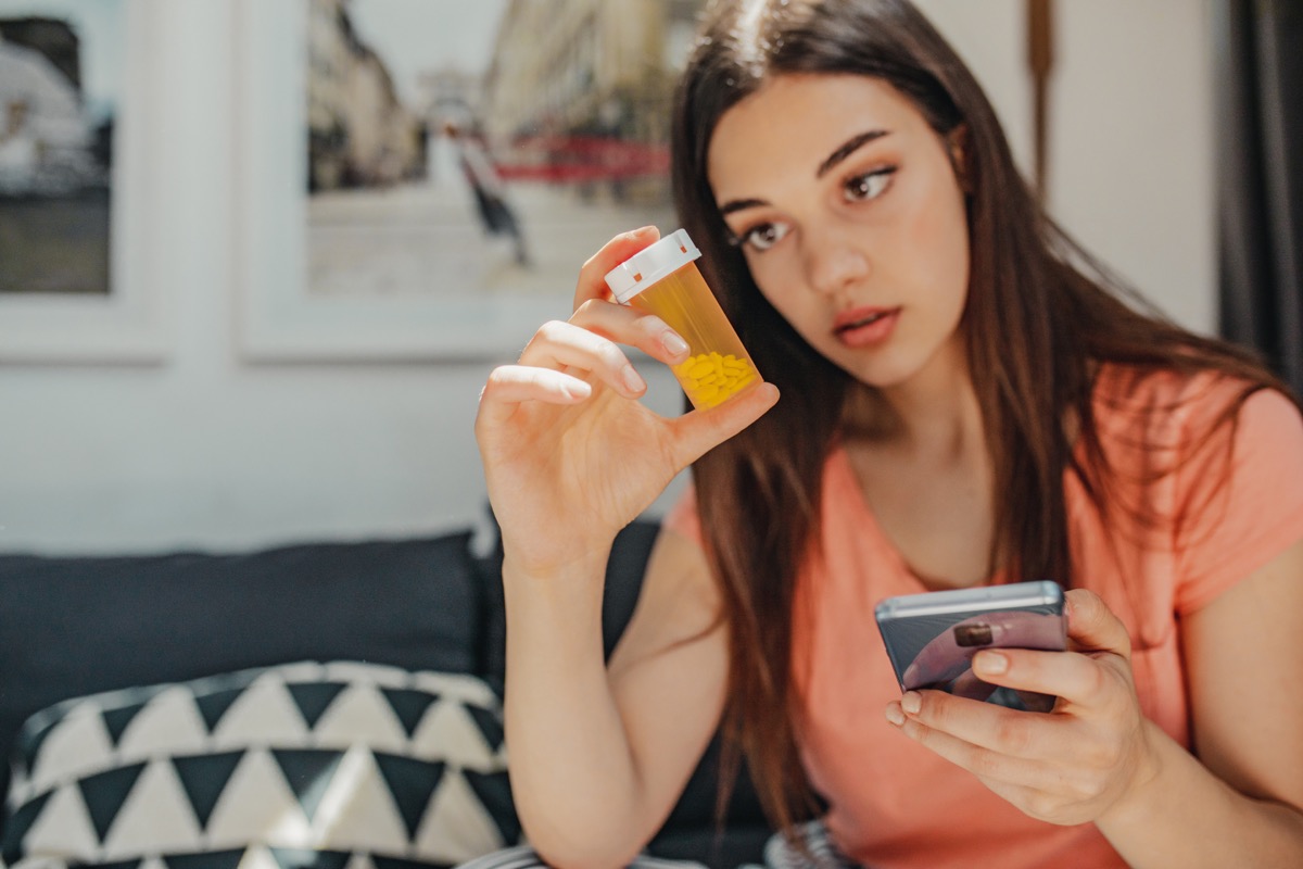 The woman is holding a mobile phone and a bottle of pills