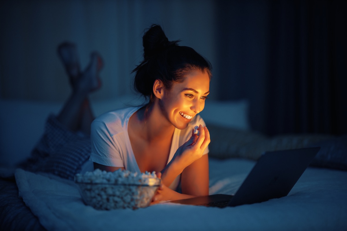 Woman eating popcorn with an open laptop