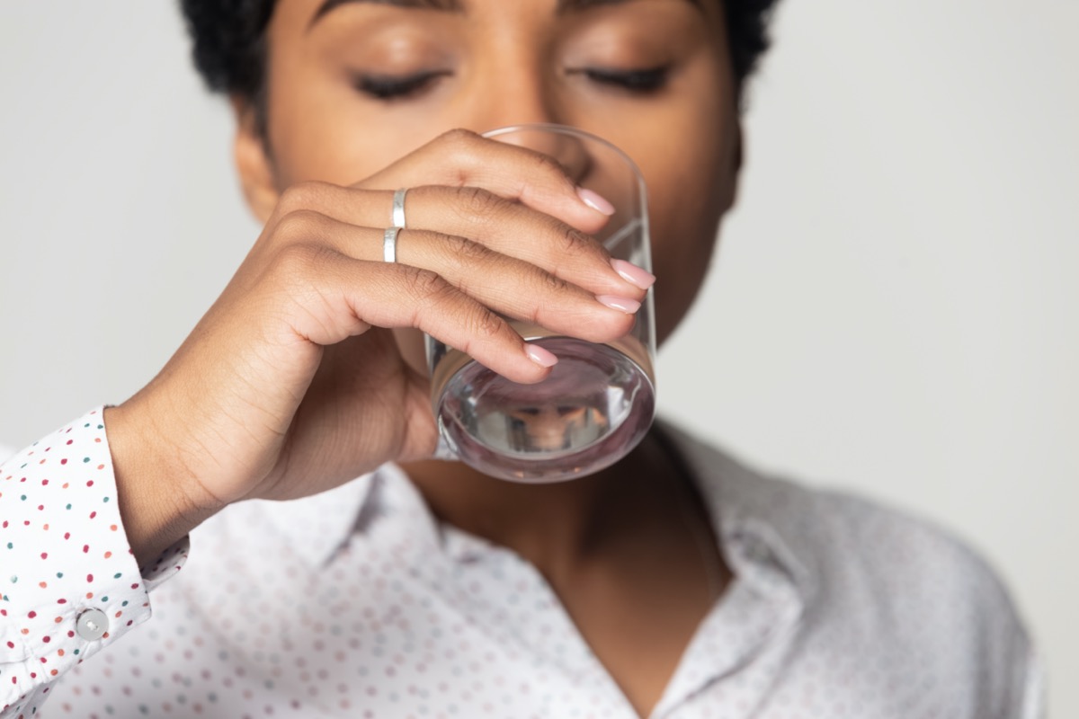 with closed eyes drinking clean mineral water close up, young woman holding a glass