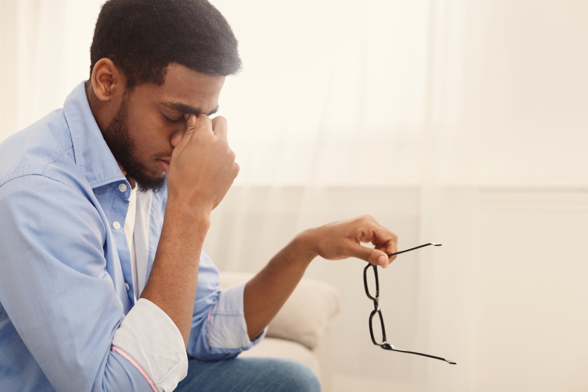 man massaging the bridge of his nose, taking off his glasses, having blurred vision or dizziness