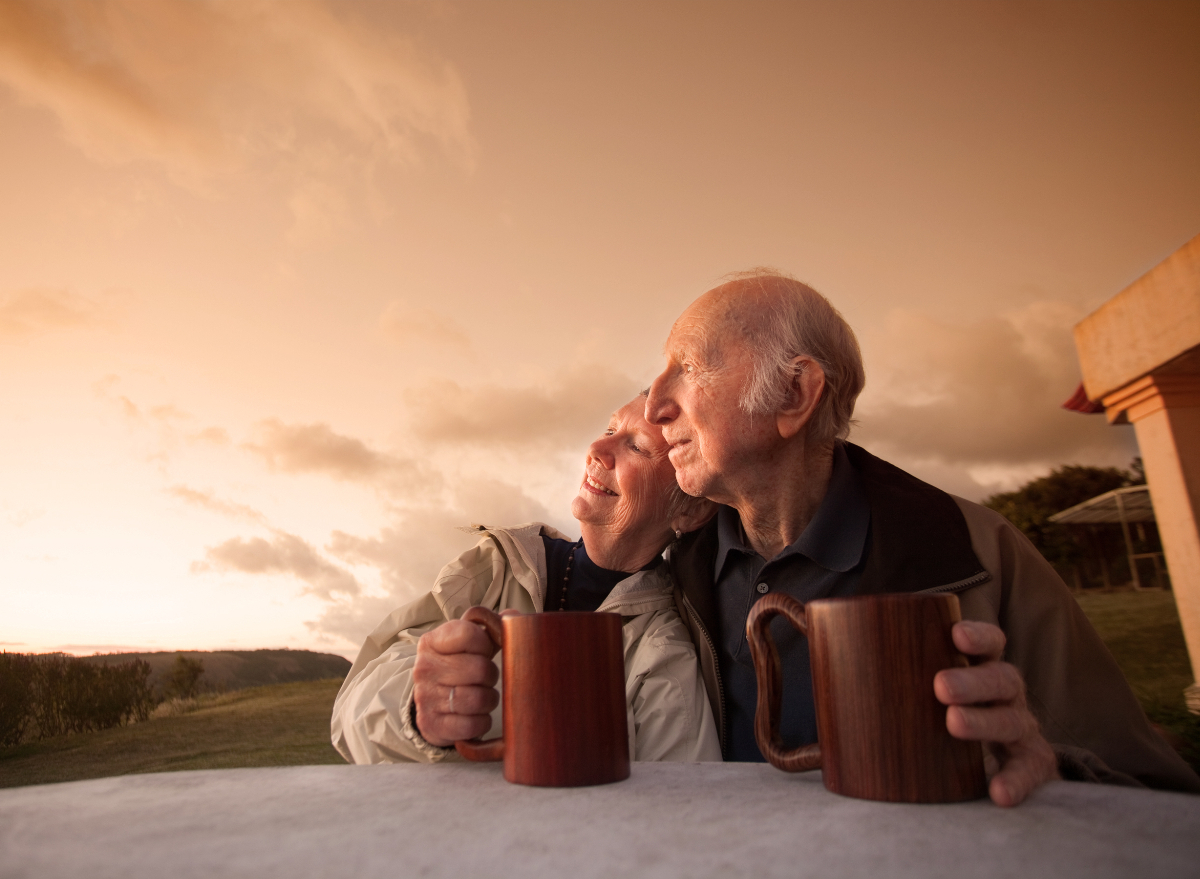 elderly couple snuggle outside while enjoying morning coffee