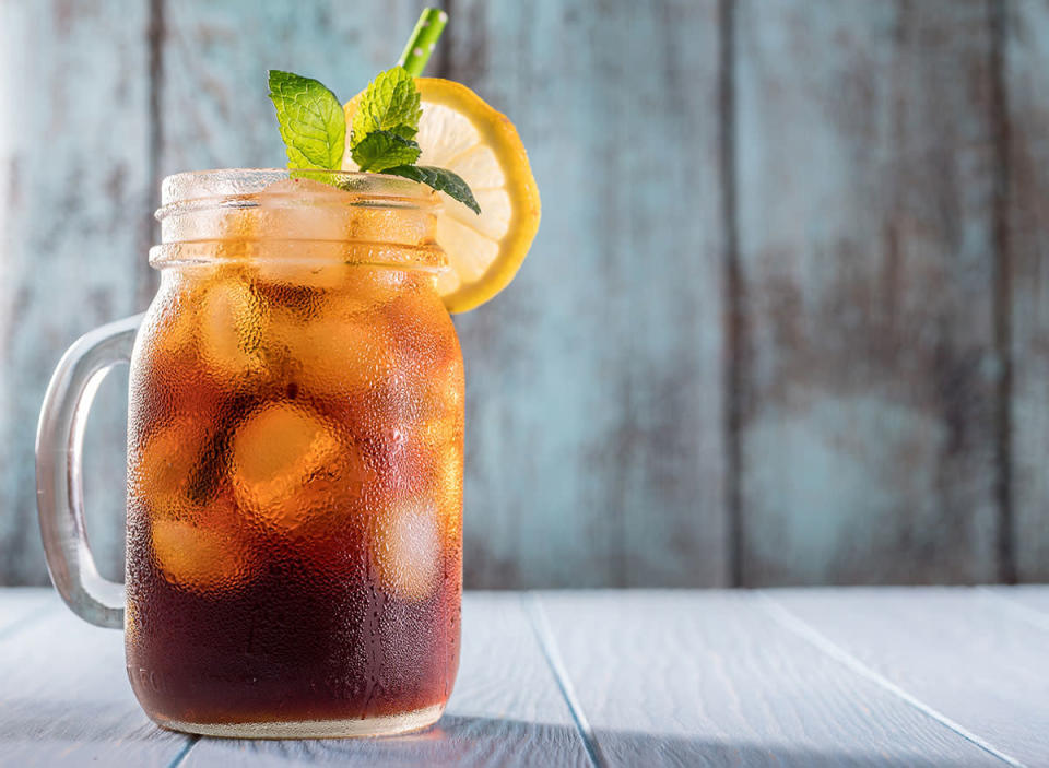 iced tea in a mason jar with a green straw, lemon wheel and a sprig of mint