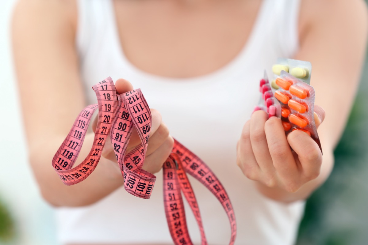 Woman holding packs of pills and tape measure in hands.