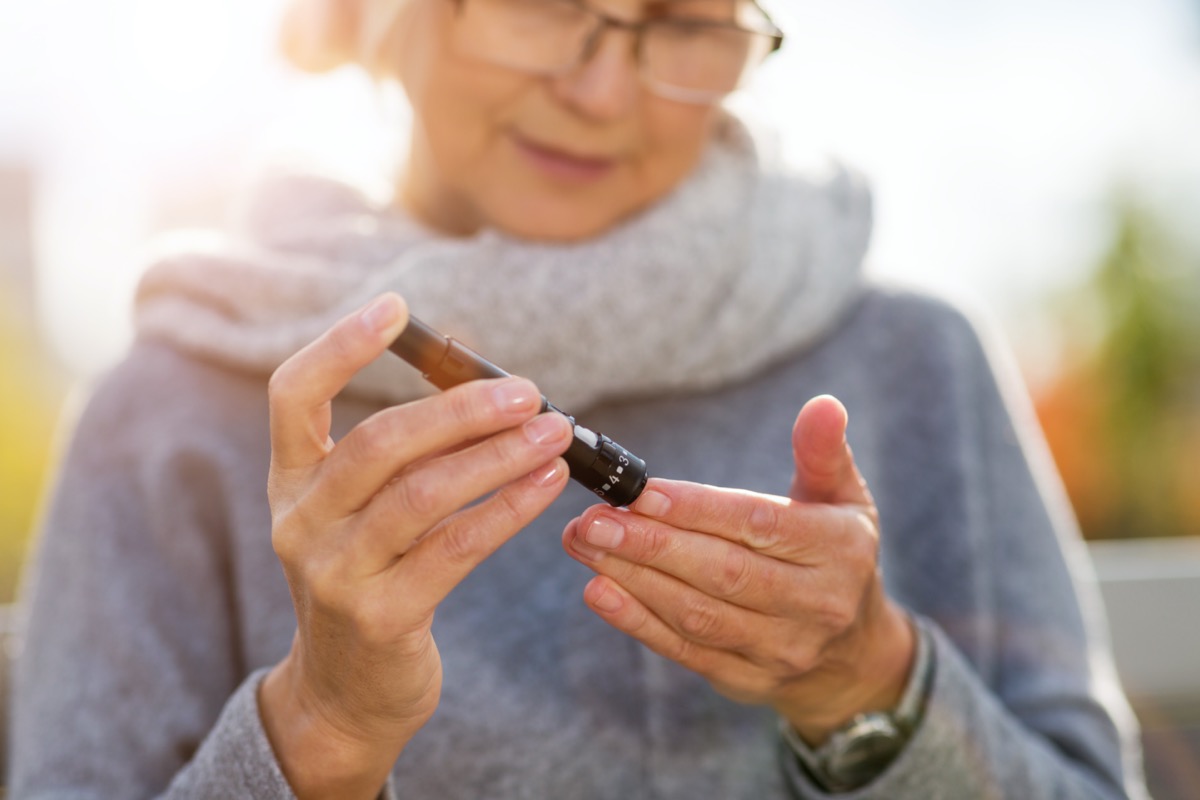 Woman checking blood sugar level while sitting on a bench