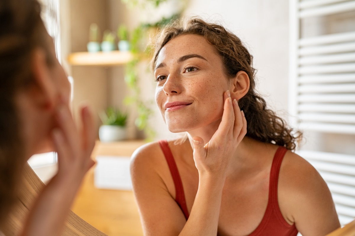 Young woman looking at the mirror while touching her face.