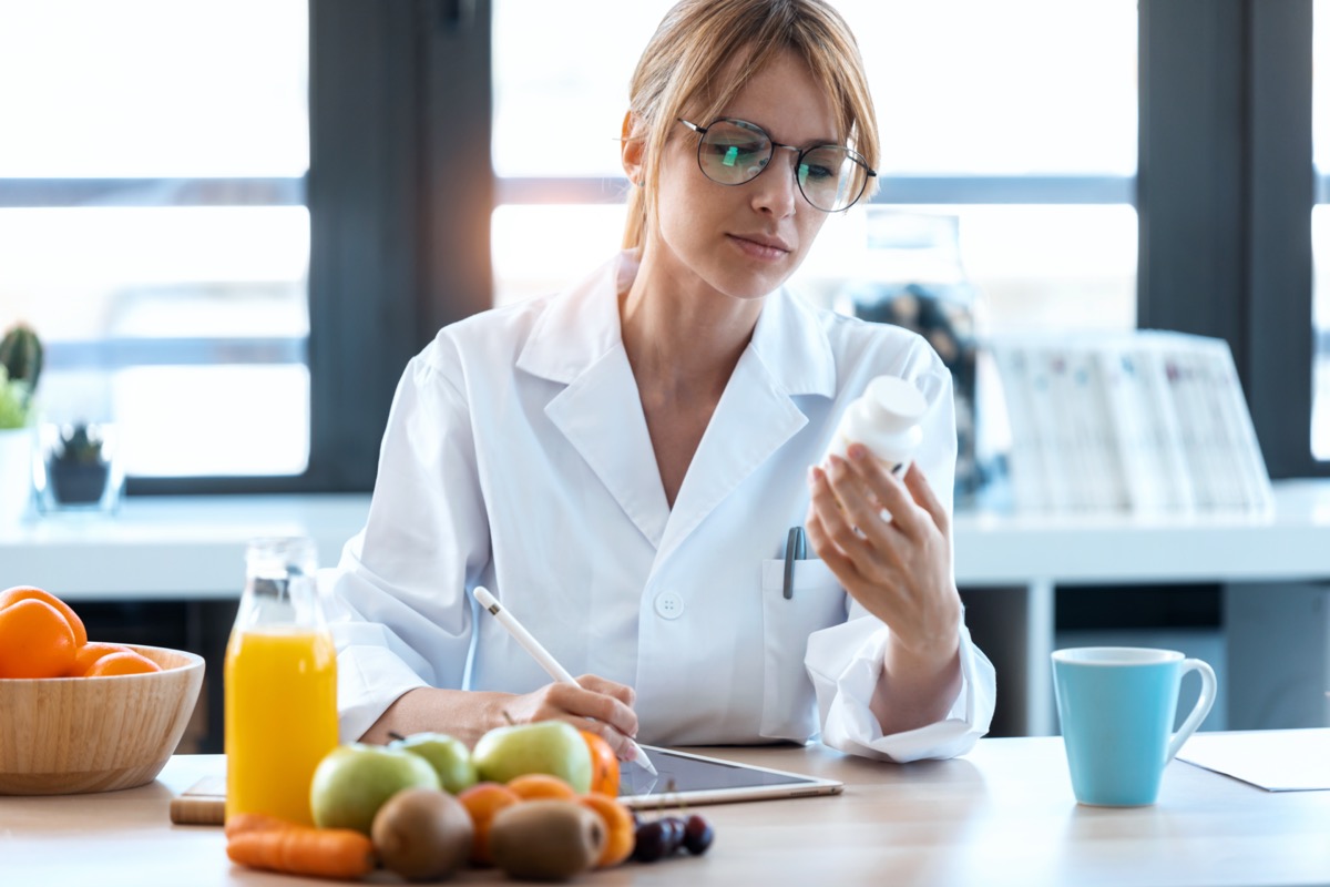 A photo of a nutritionist doctor writes the medical prescription for a correct diet on a desk with fruits, pills and supplements.