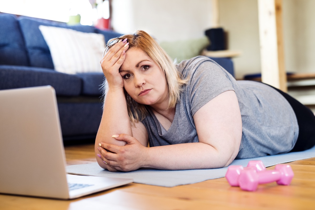 overweight woman at home lying on the floor, laptop in front of her, ready to exercise on the mat according to the video