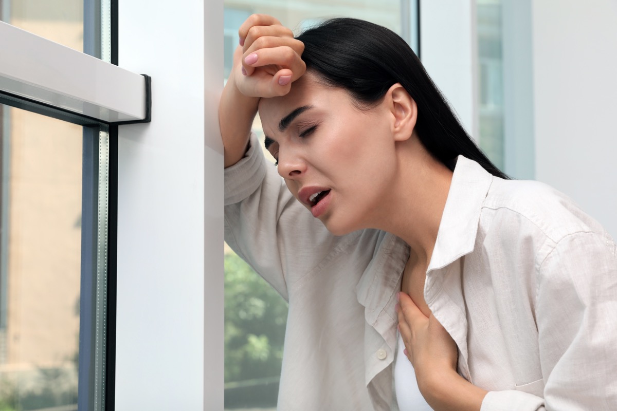 Young woman suffering from breathing problems near the window indoors.