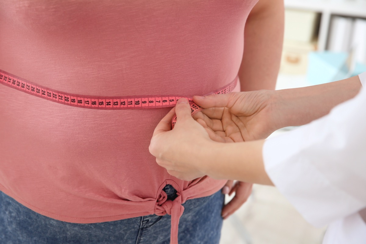 Female doctor measuring waist of overweight woman with measuring tape in clinic