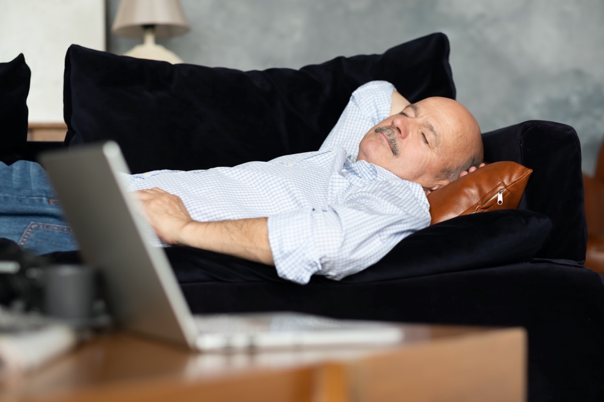 Tired elderly Hispanic man sleeping on a dark blue sofa, taking a nap in the living room