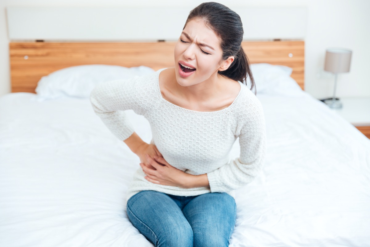 Woman sitting on bed and touching her left side in pain at home