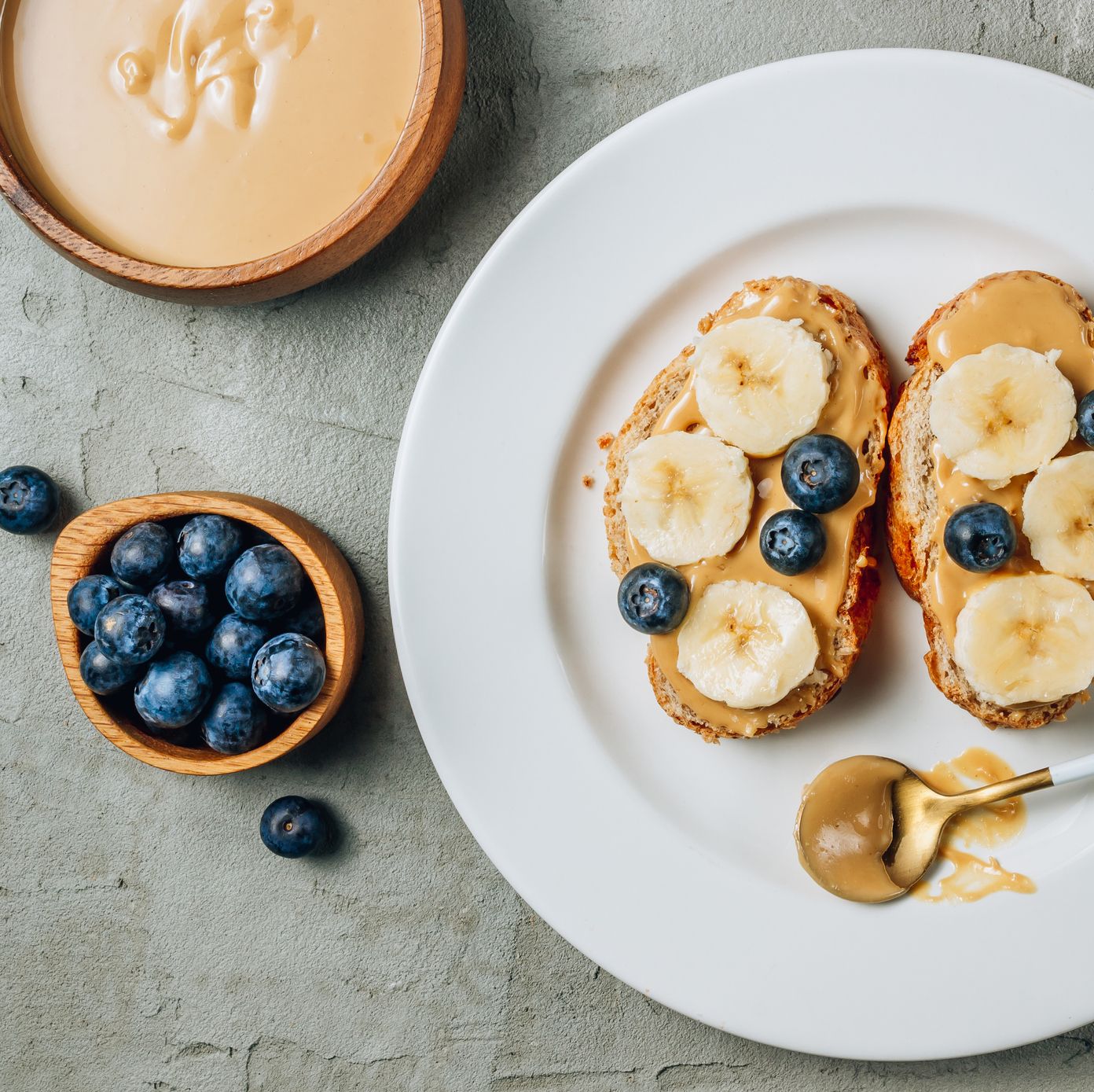 healthy buckwheat bread with peanut butter, banana and blueberries on a white plate on a concrete background top view flat lay summer breakfast