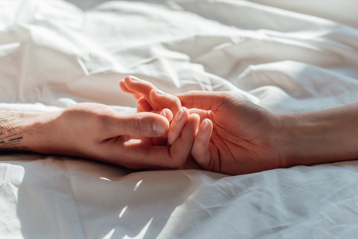 live couple holding hados while lying in bed together