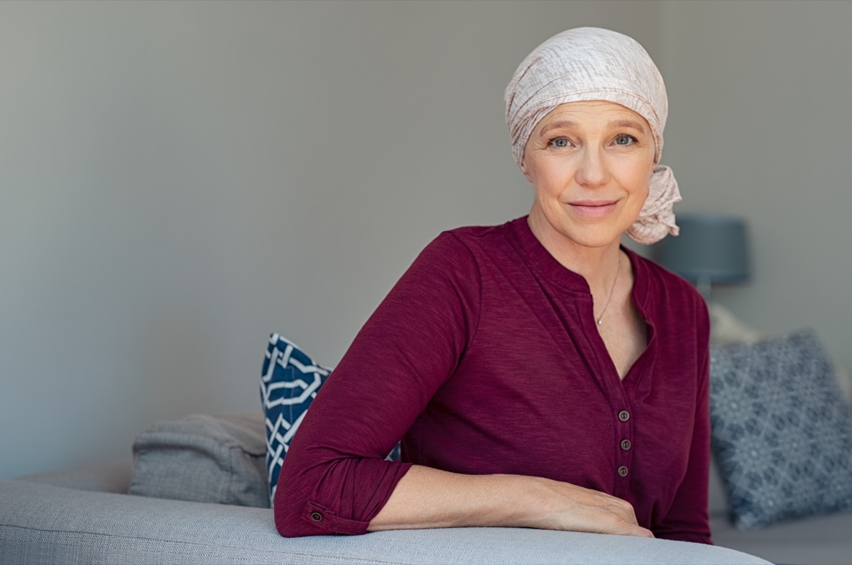 Cancer mature woman in pink headscarf smiling sitting on sofa at home