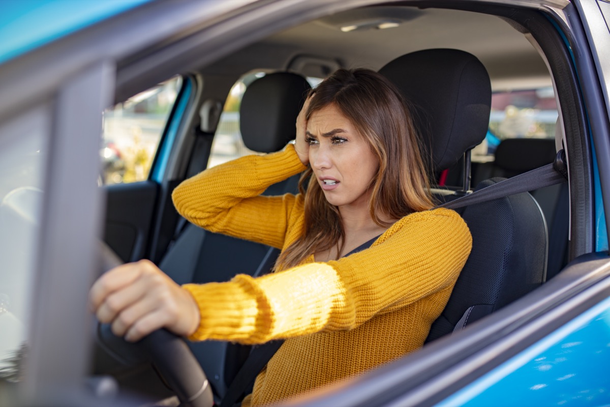 The female driver sits behind the wheel in the car, touches her head.