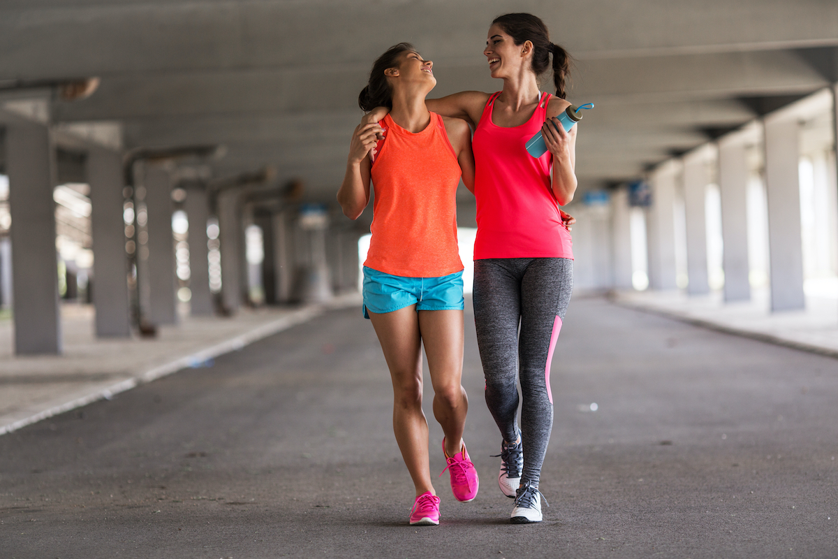 A couple of girlfriends jogging on the city street under the overpass of the city road.  They relax after jogging and teasing.  Hugging each other.  Walkers