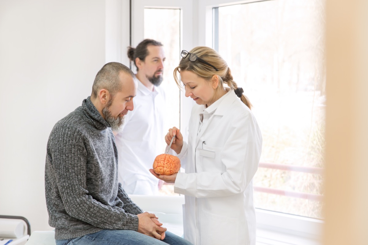 a female neurologist is showing a male patient something on a synthetic brain