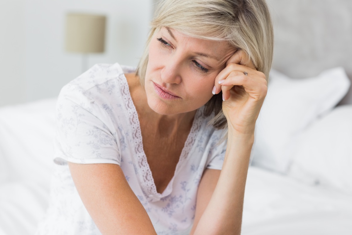 Mature woman sitting on bed at home.