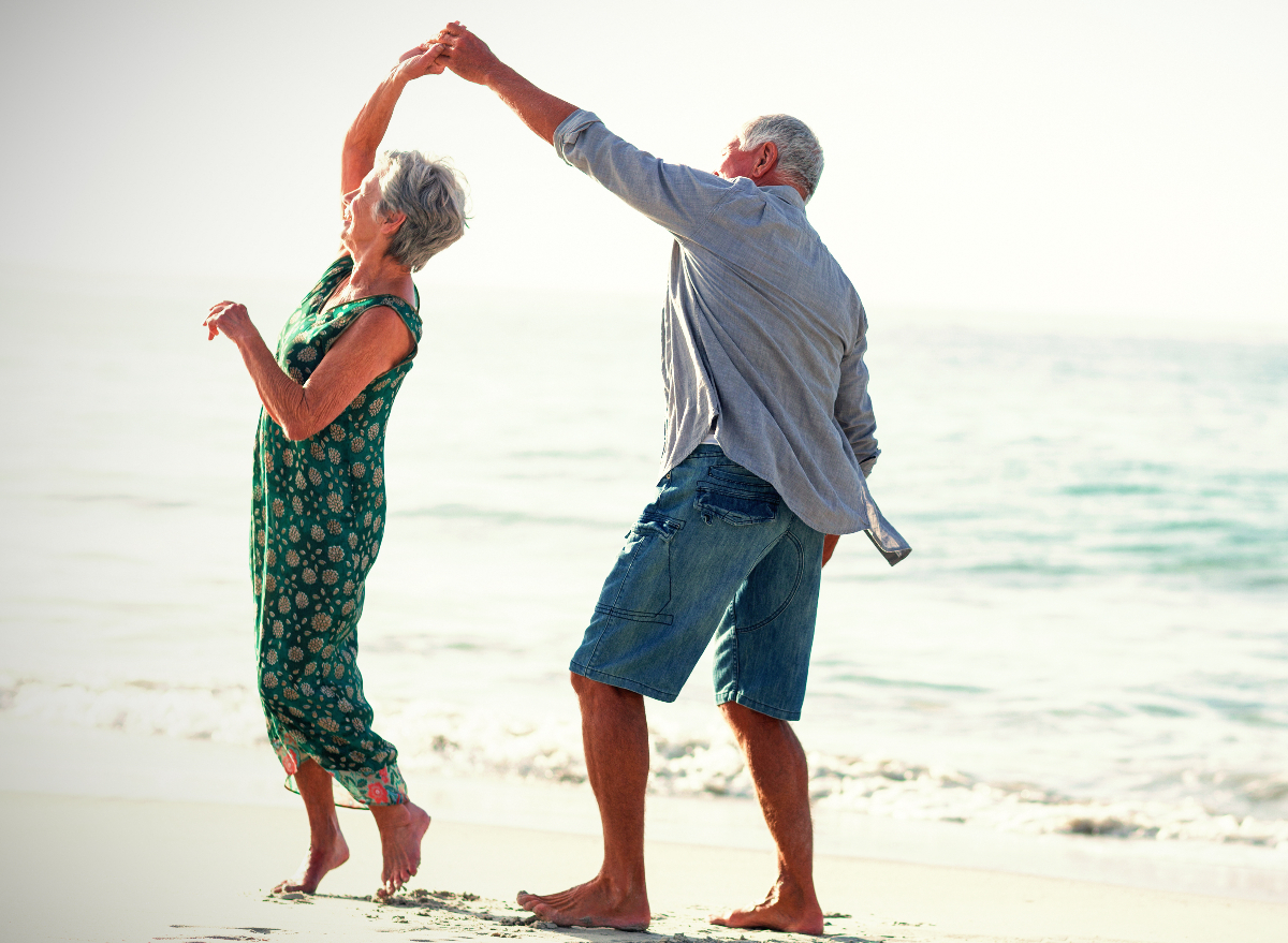 happy elderly couple dance on the beach